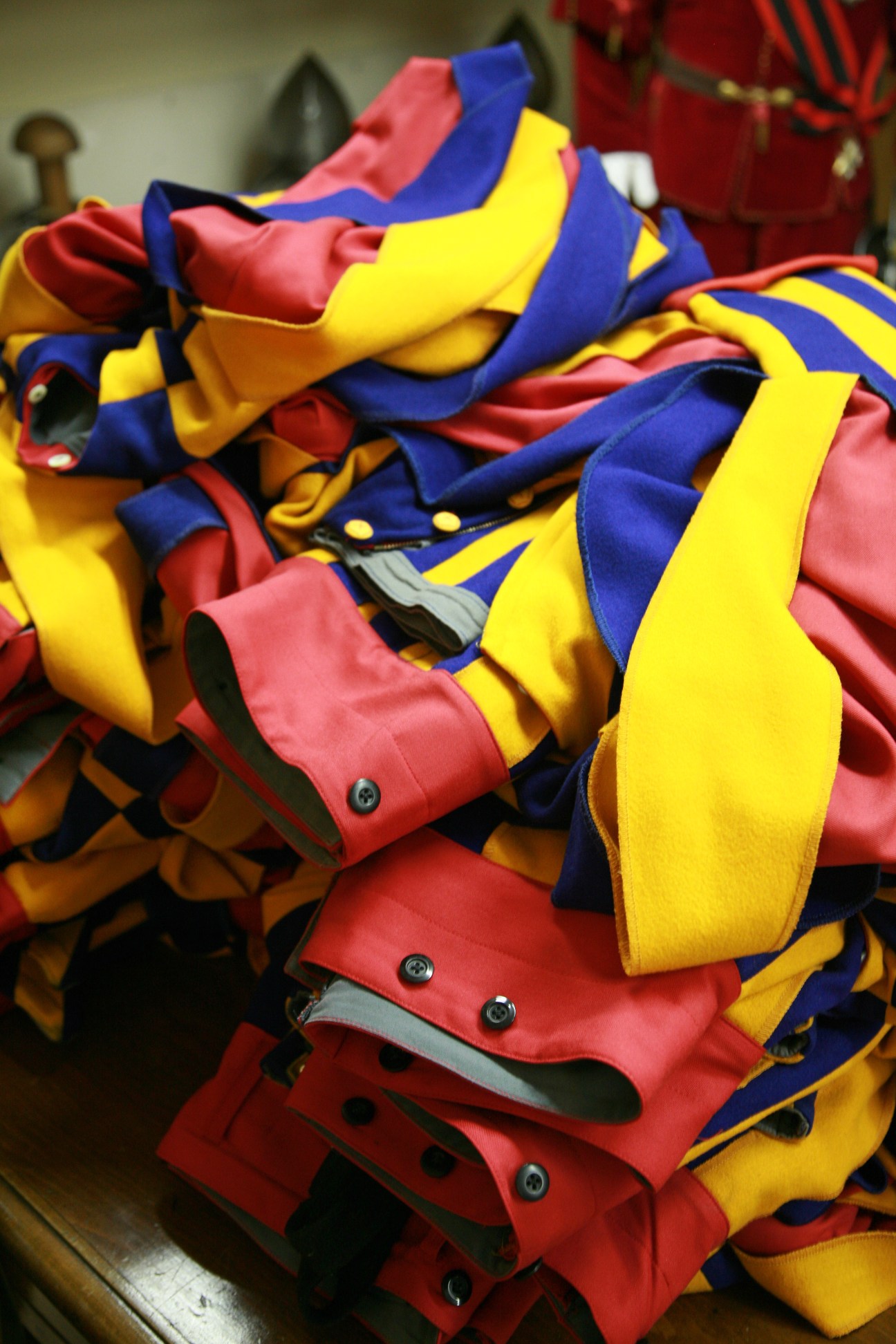 Pile of completed Swiss Guard dress uniforms in blue, yellow and red striped fabric with brass buttons.