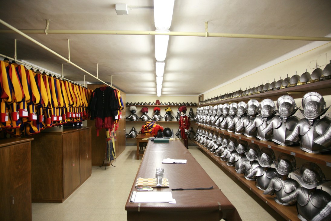Swiss Guards armoury displaying striped uniforms on left wall and polished metal helmets on right shelves.