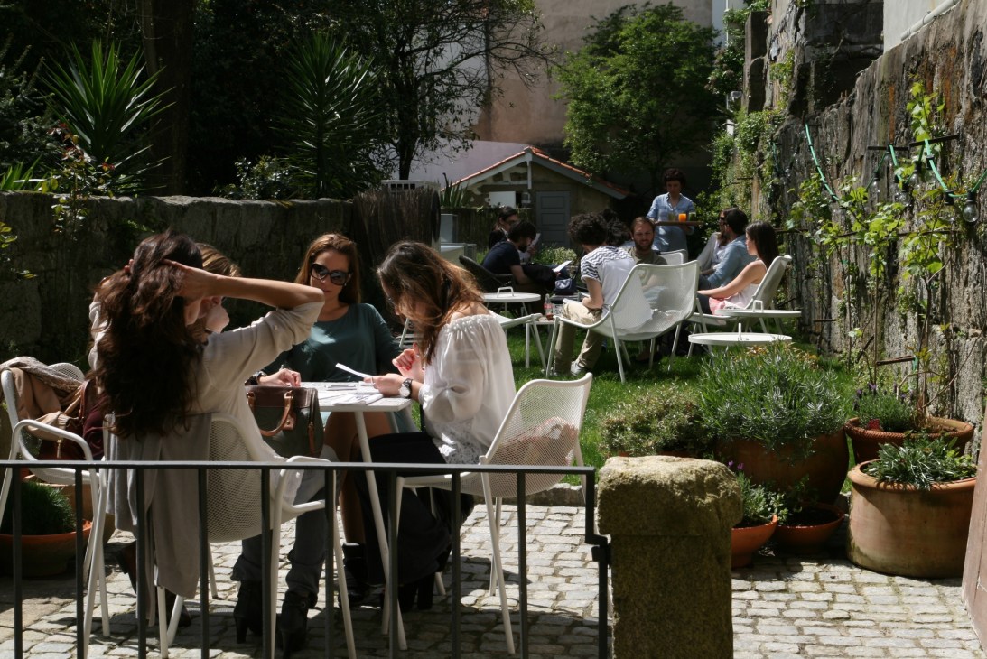 Guests dining in a sunny courtyard at Rosa Et Al with ivy-covered stone walls and potted plants.