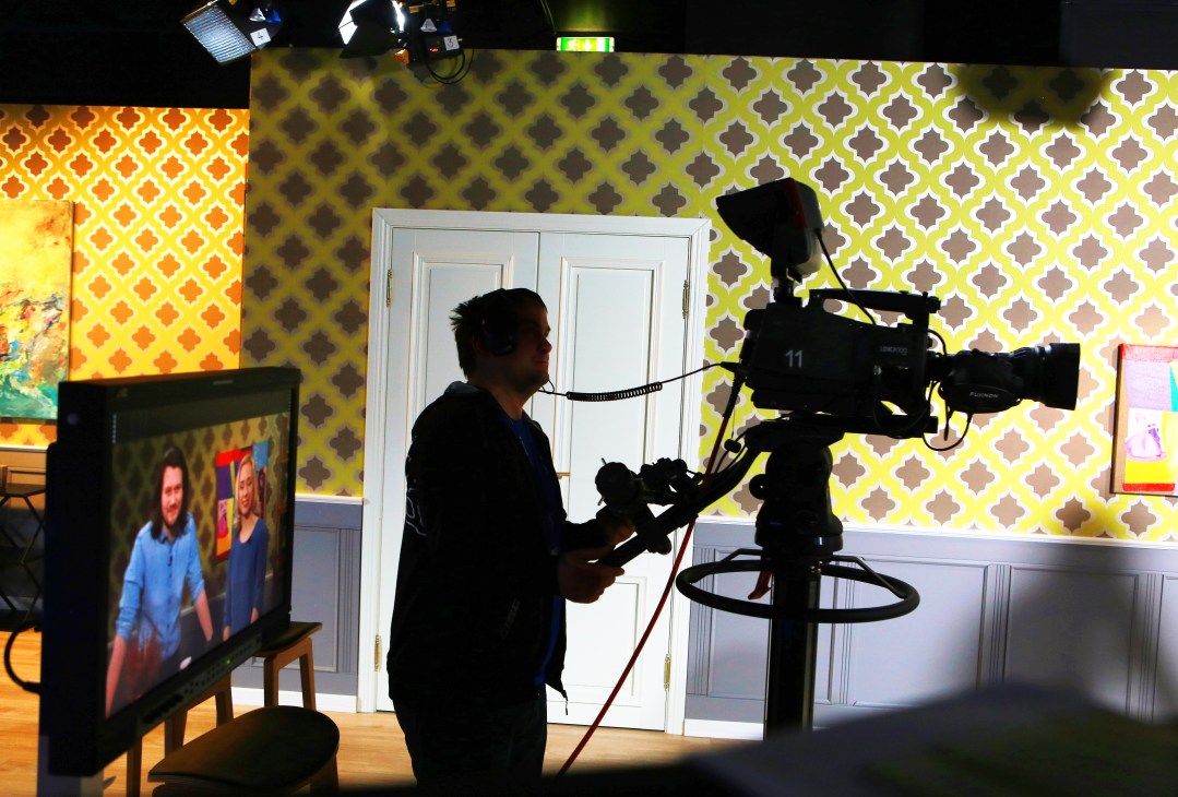 Cameraman filming a television studio set with patterned yellow and brown backdrop for the morning show Coffee+.