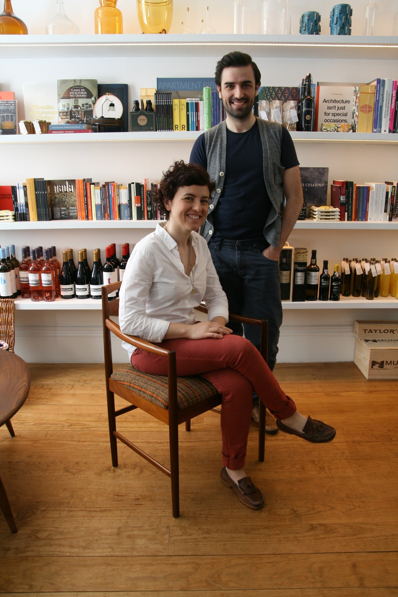 Two people posing in front of shelving displaying bottles and books at Rosa Et Al in Porto.