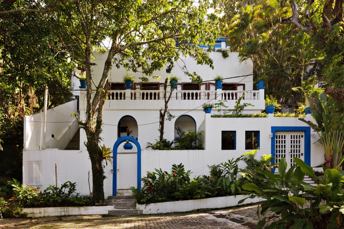 White modernist Rio residence with blue architectural details surrounded by lush tropical vegetation.