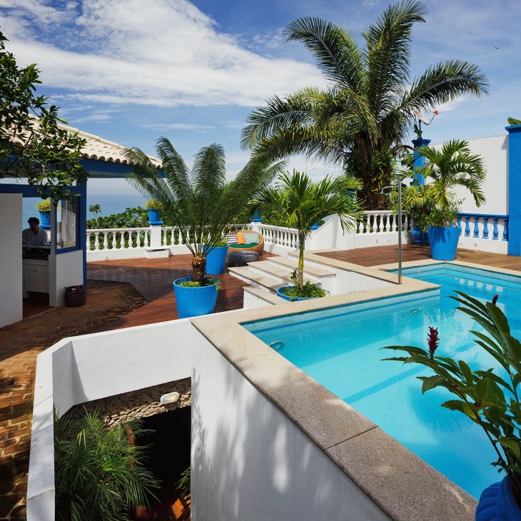 Rio residence pool with terraced deck, white balustrade railings, palm trees, and blue accents overlooking the Atlantic Ocean.