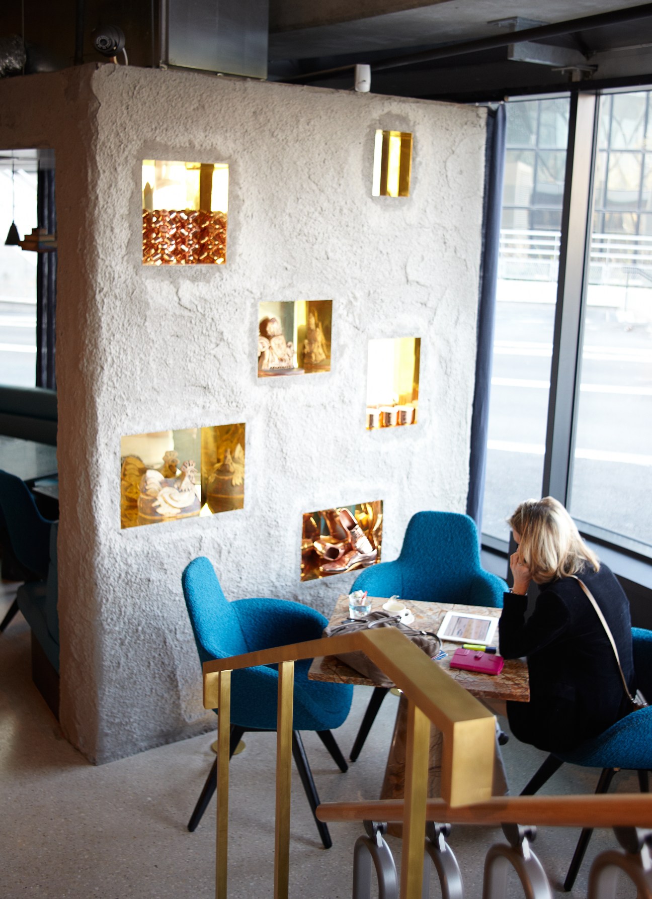 Interior of Restaurant Éclectic showing a woman seated at a table with blue chairs beside a white textured wall with illuminated photo frames.