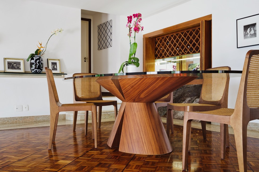 Dining area with wooden table and cane chairs, hardwood flooring, and marble wine cabinet built into stone wall.