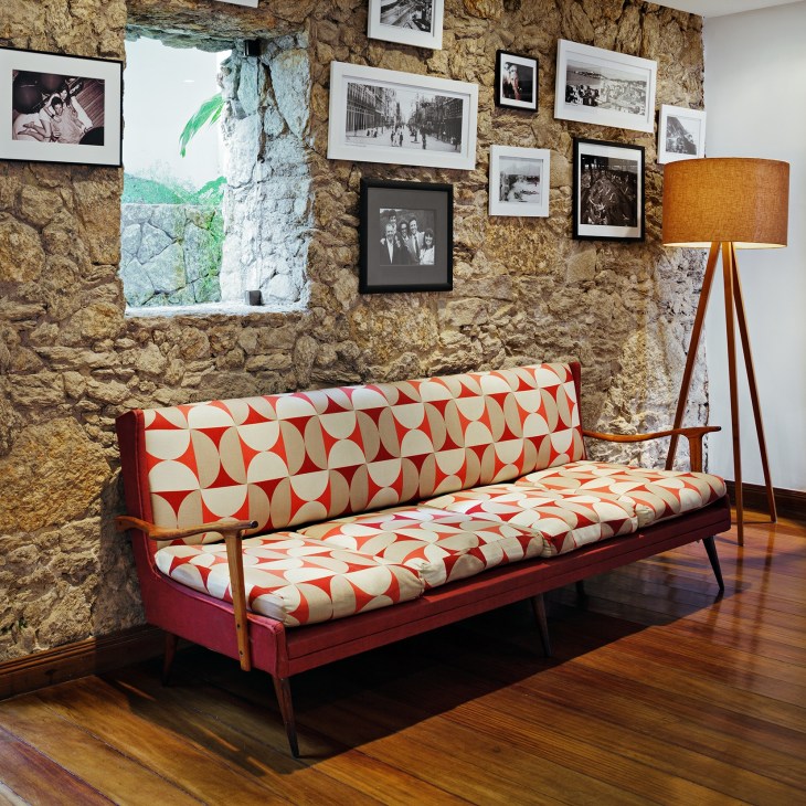 Vintage Brazilian sofa with red and cream geometric pattern against a stone wall with framed photographs.