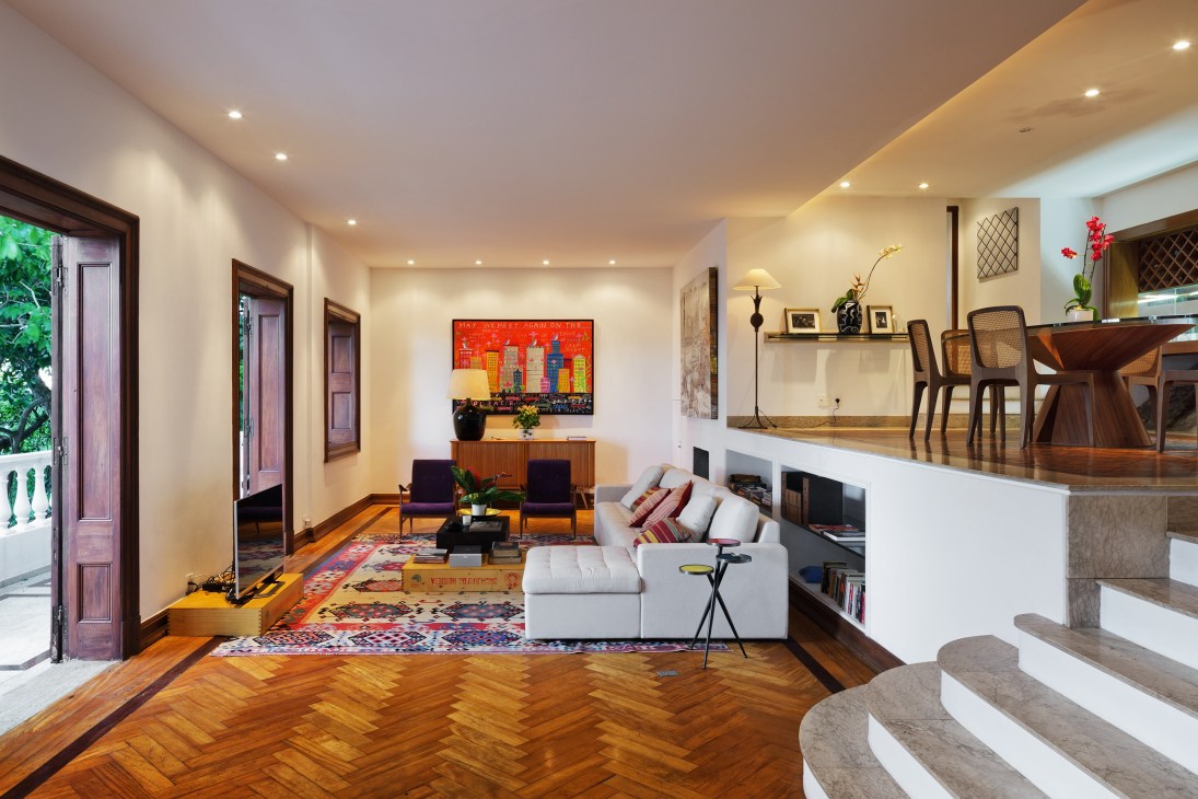 Living area with white sofa, mid-century chairs, hardwood flooring, and colorful artwork on walls