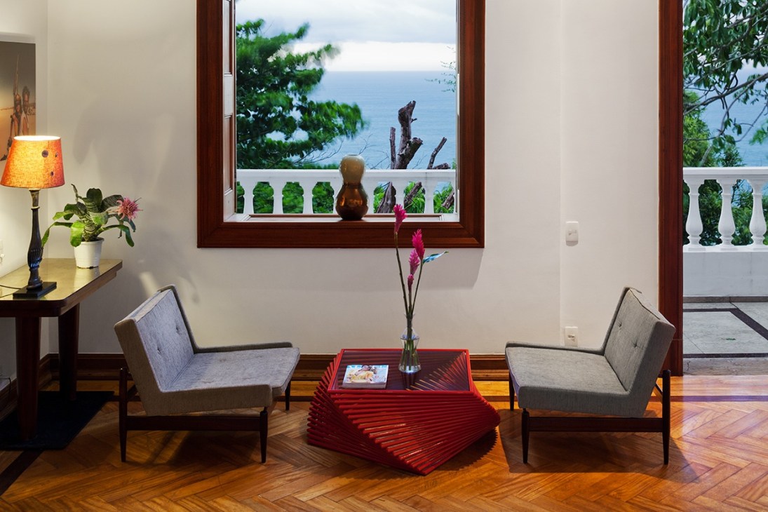 Rio residence veranda with mid-century chairs, ocean views through large windows with white balustrade railing.