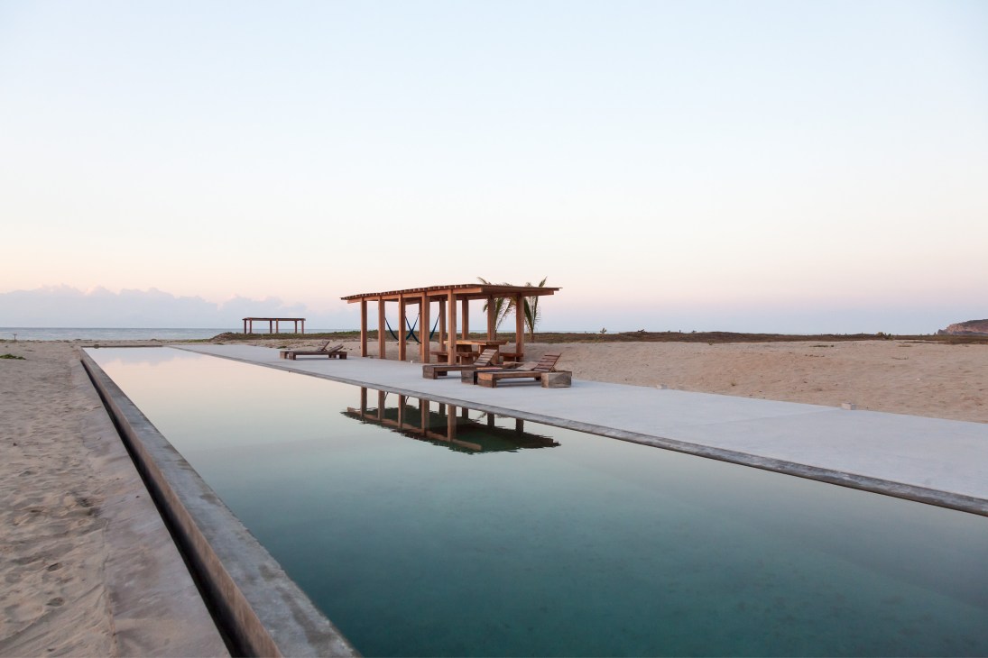 Pool area at Casa Wabi artists' residency at sunrise with wooden pergola and beach pavilion structures.