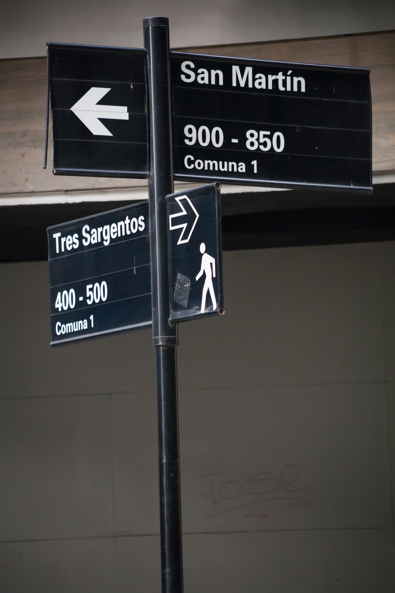 Black street signage in Buenos Aires showing directional arrows, street names and house numbers in white Helvetica typeface.