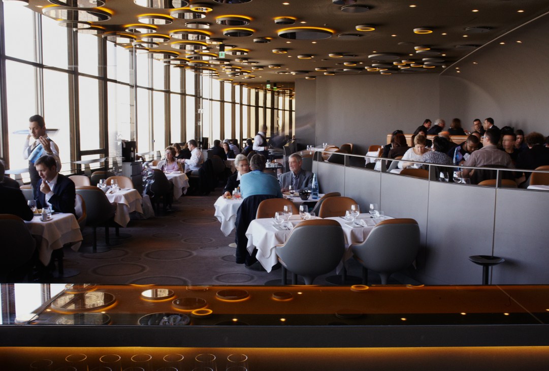 Le Ciel de Paris restaurant interior with UFO-like amber ceiling lights and diners at tables with city views.