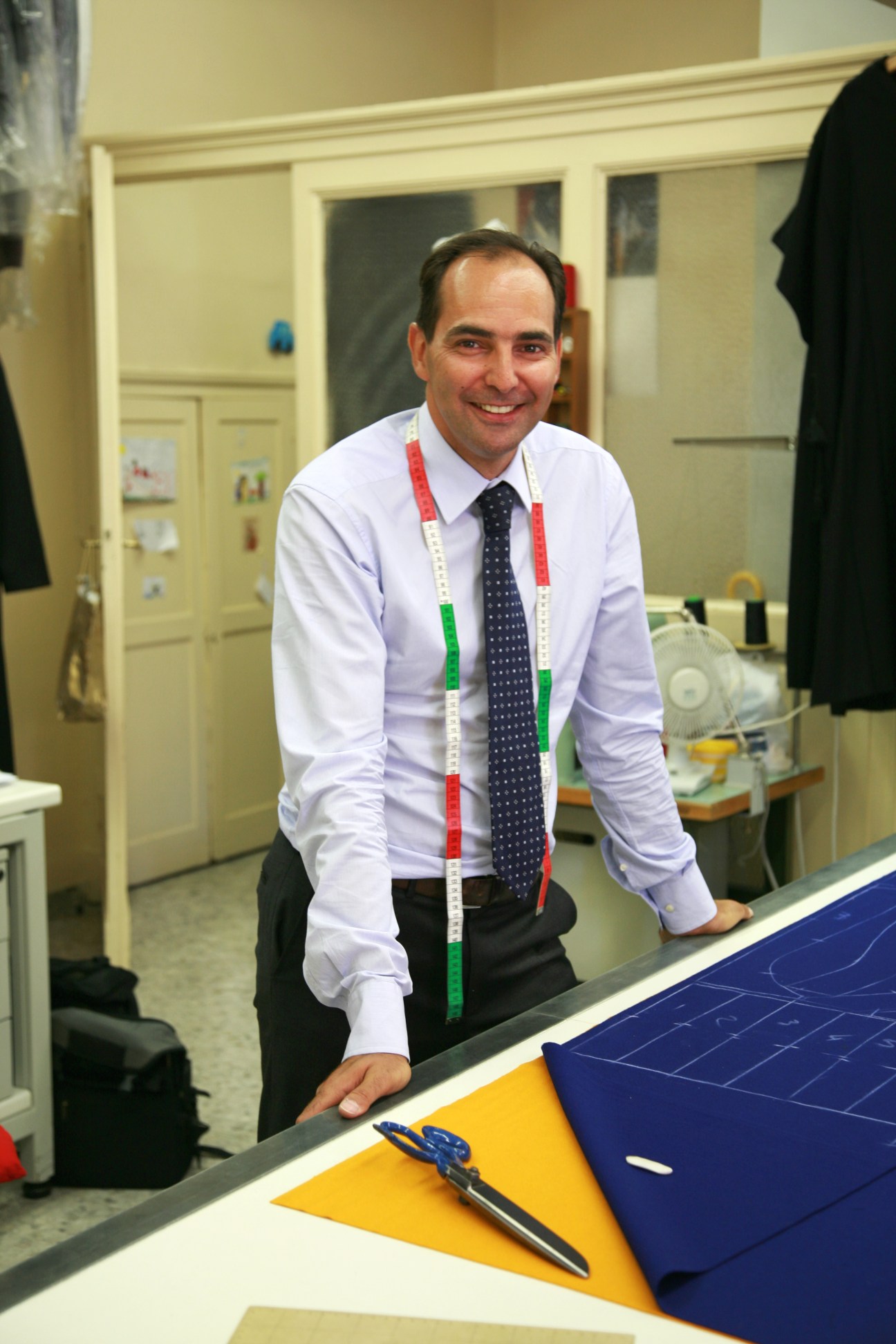 Tailor Ety Cicioni smiles while working at his table in the Vatican atelier with fabric samples.