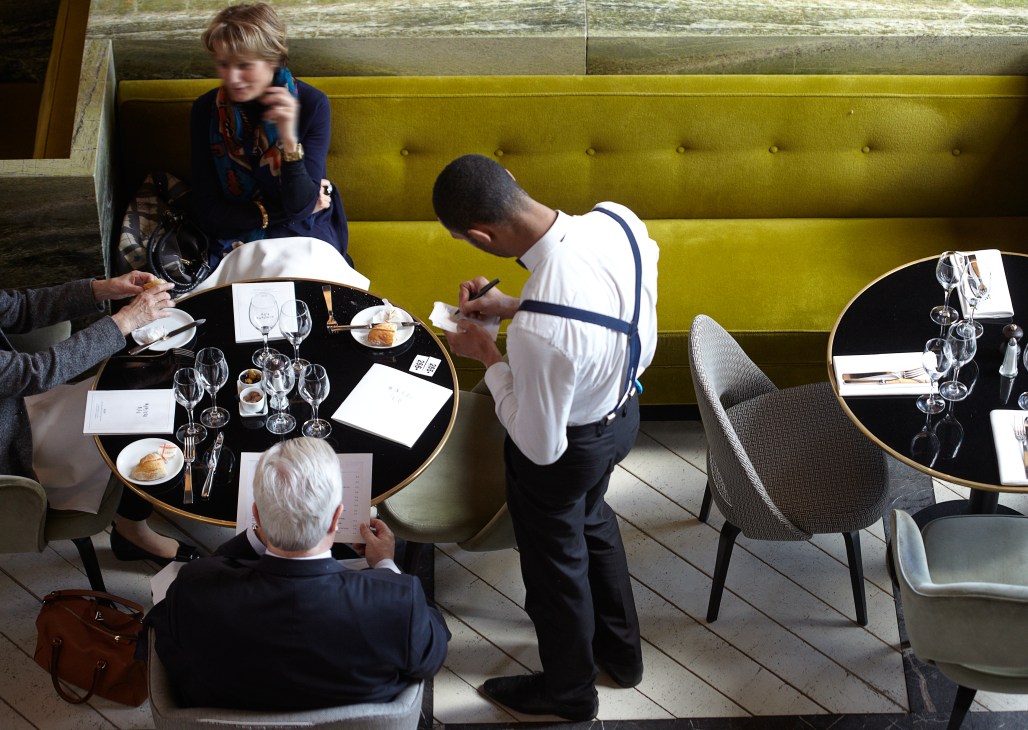 Waiter serves diners at a table with chartreuse banquette seating in a modern restaurant.