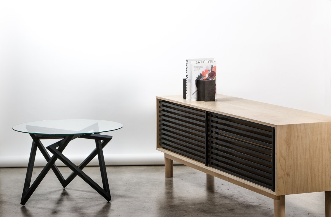 Wooden sideboard with black lattice-work doors and a glass-topped table with black metal base in a minimalist interior.