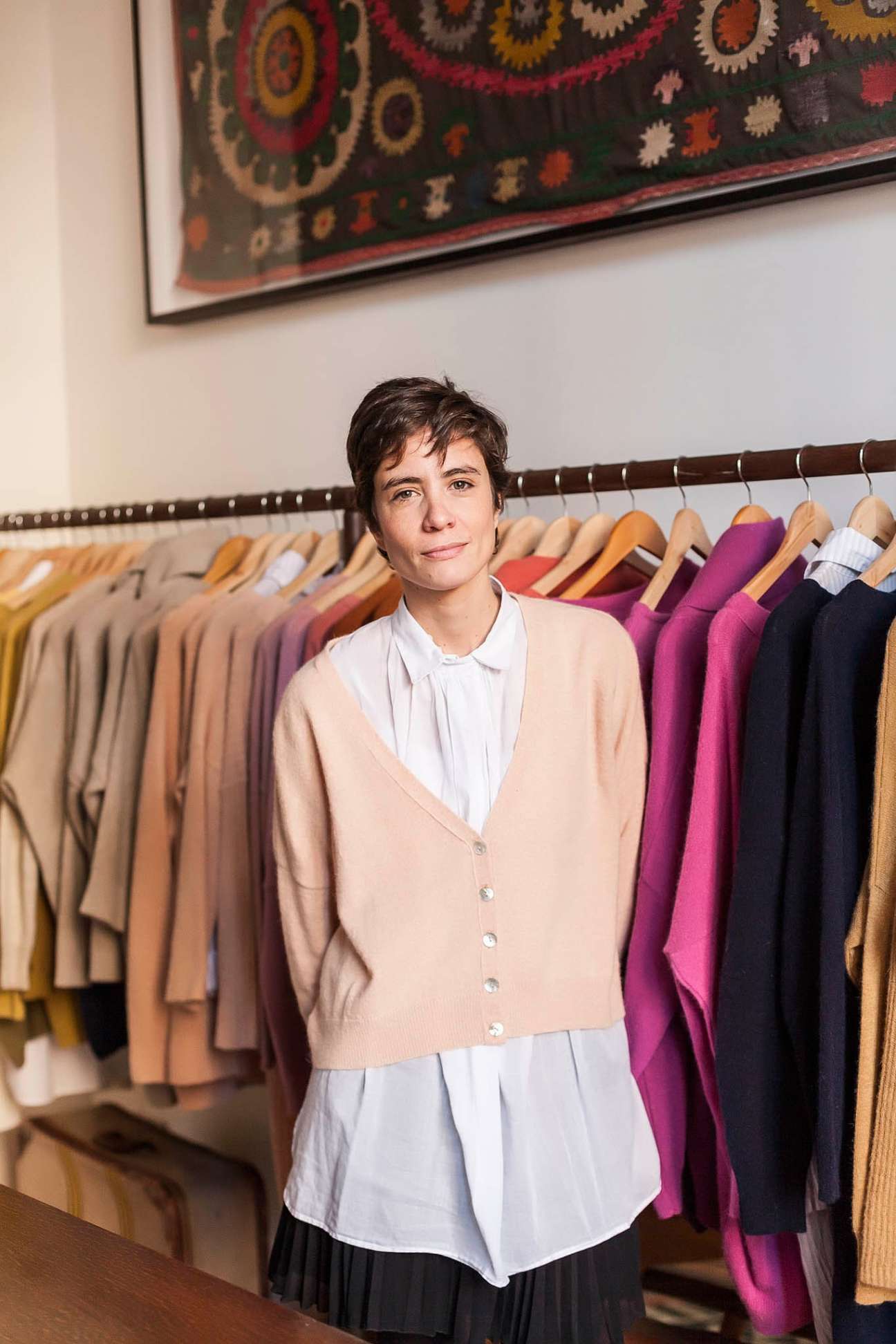 Cata Chavanne, founder of Blue Sheep, stands in front of colorful wool cardigans and jumpers hanging on a rail in her boutique.