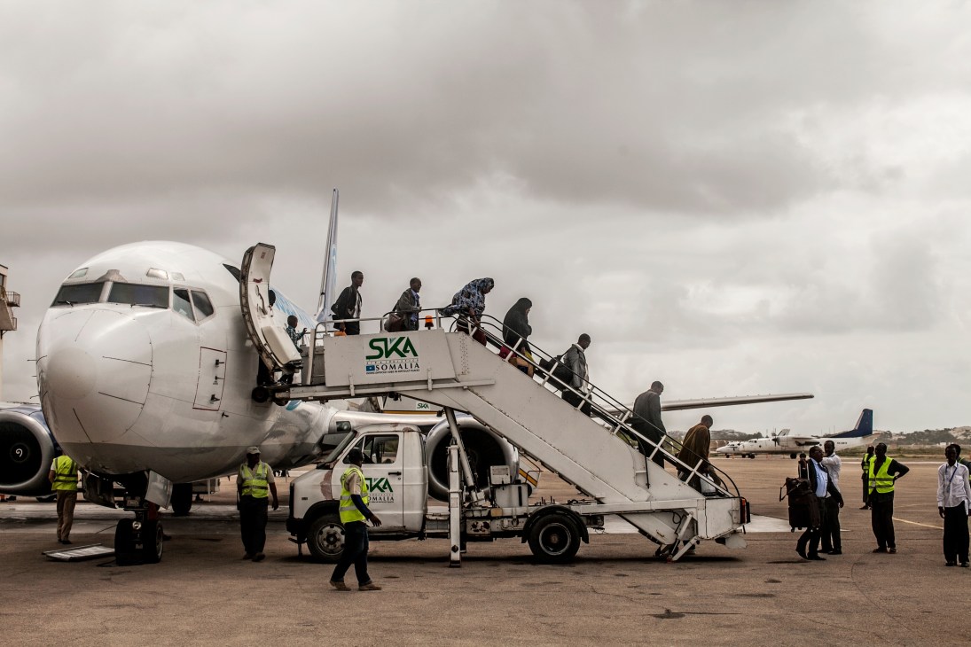 Passengers disembark from a SKA Somalia aircraft via stairs at Mogadishu airport with ground staff in high-visibility vests nearby.