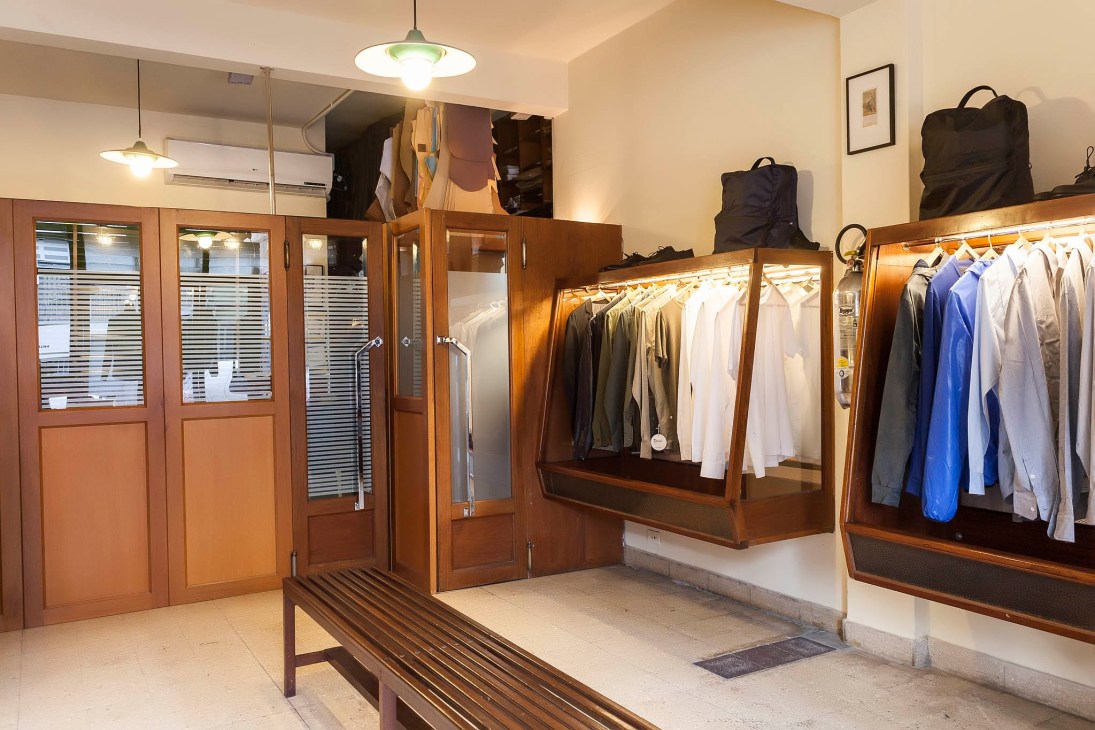 Interior of Hermanos Estebecorena menswear shop with wooden display cases, hanging garments, and vintage tailor's furniture.