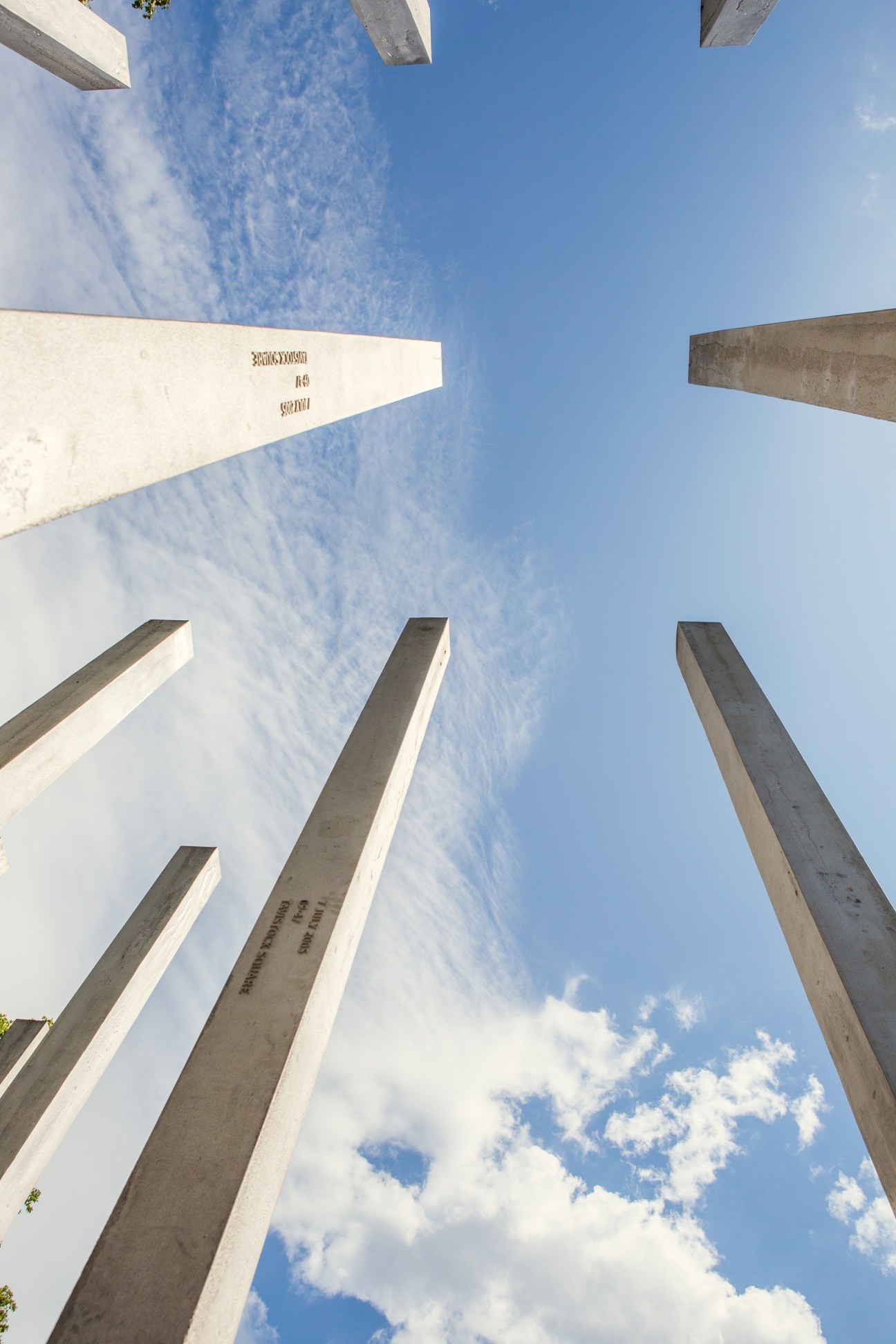 Upward view of stainless steel memorial stelae in Hyde Park, London, against blue sky.