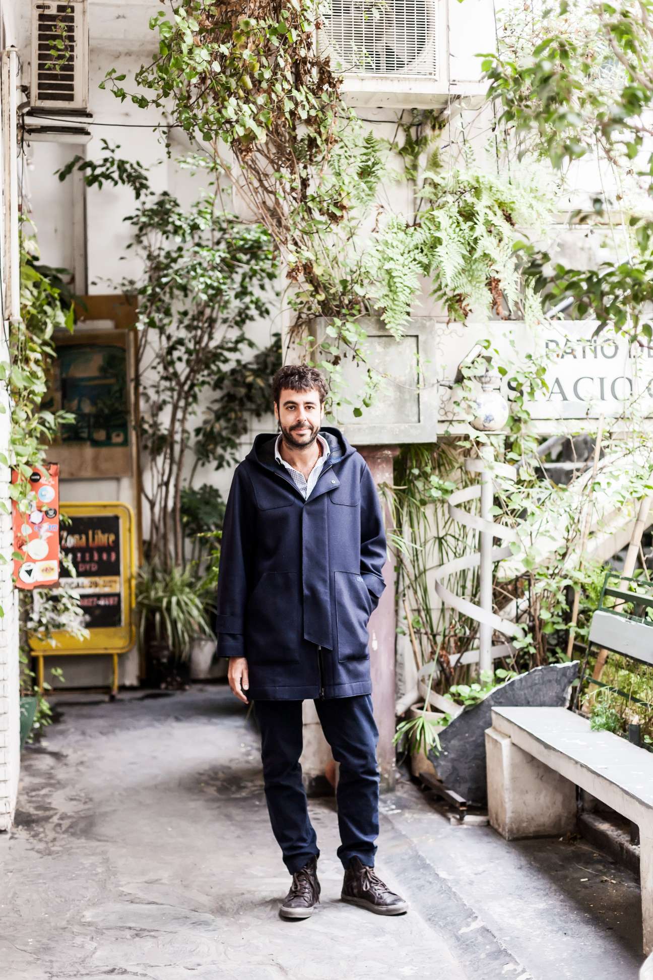 Man in navy hoodie stands in plant-filled courtyard at Galería Patio del Liceo