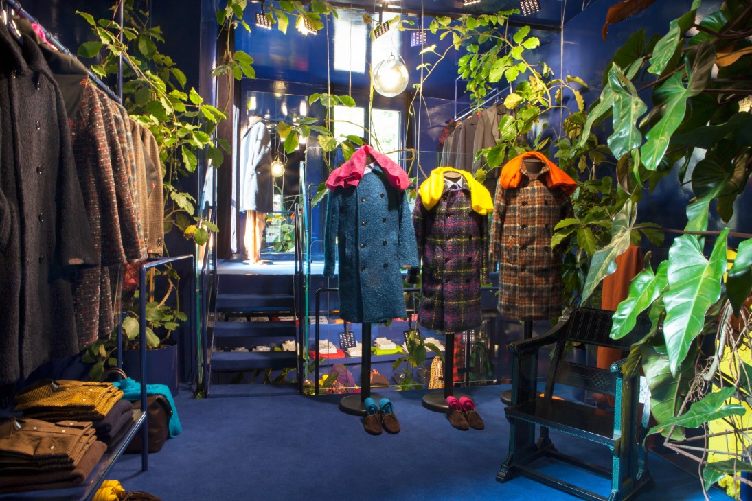 Massimo Piombo boutique interior with colorful coats on display among hanging greenery and pendant lights.