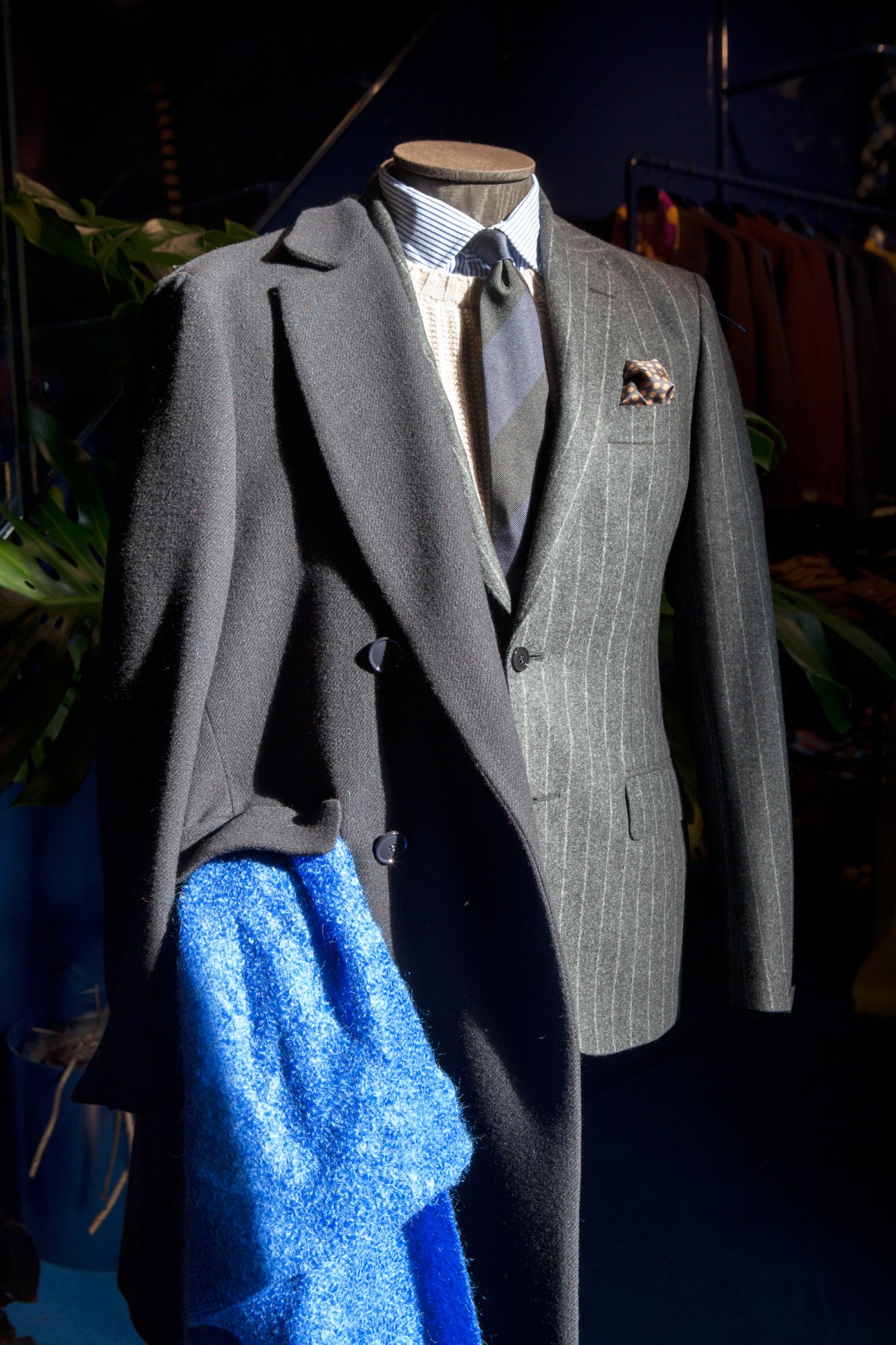 Mannequin wearing a grey Prince of Wales checked overcoat with blue textured trousers and striped shirt.