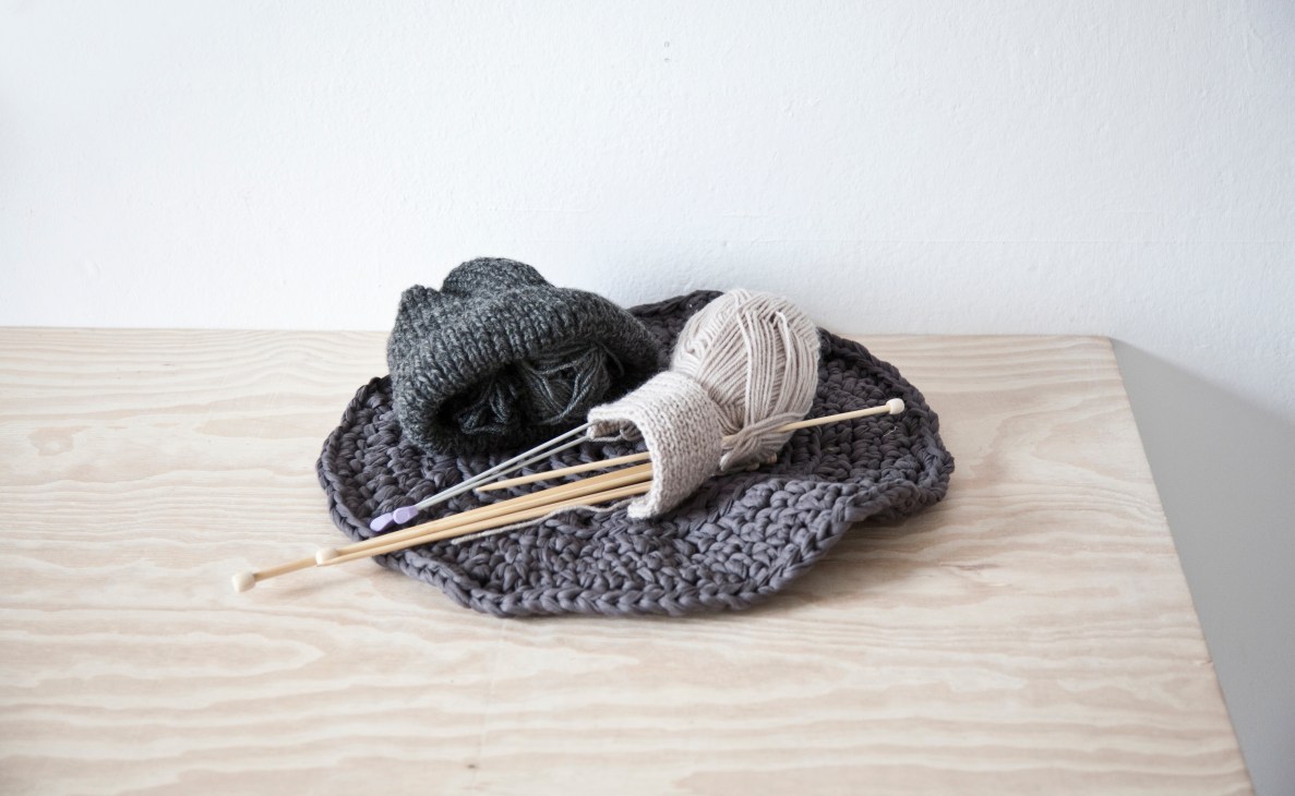 Hand-sewn textiles including knitted items and yarn on a wooden surface for Thisispaper.
