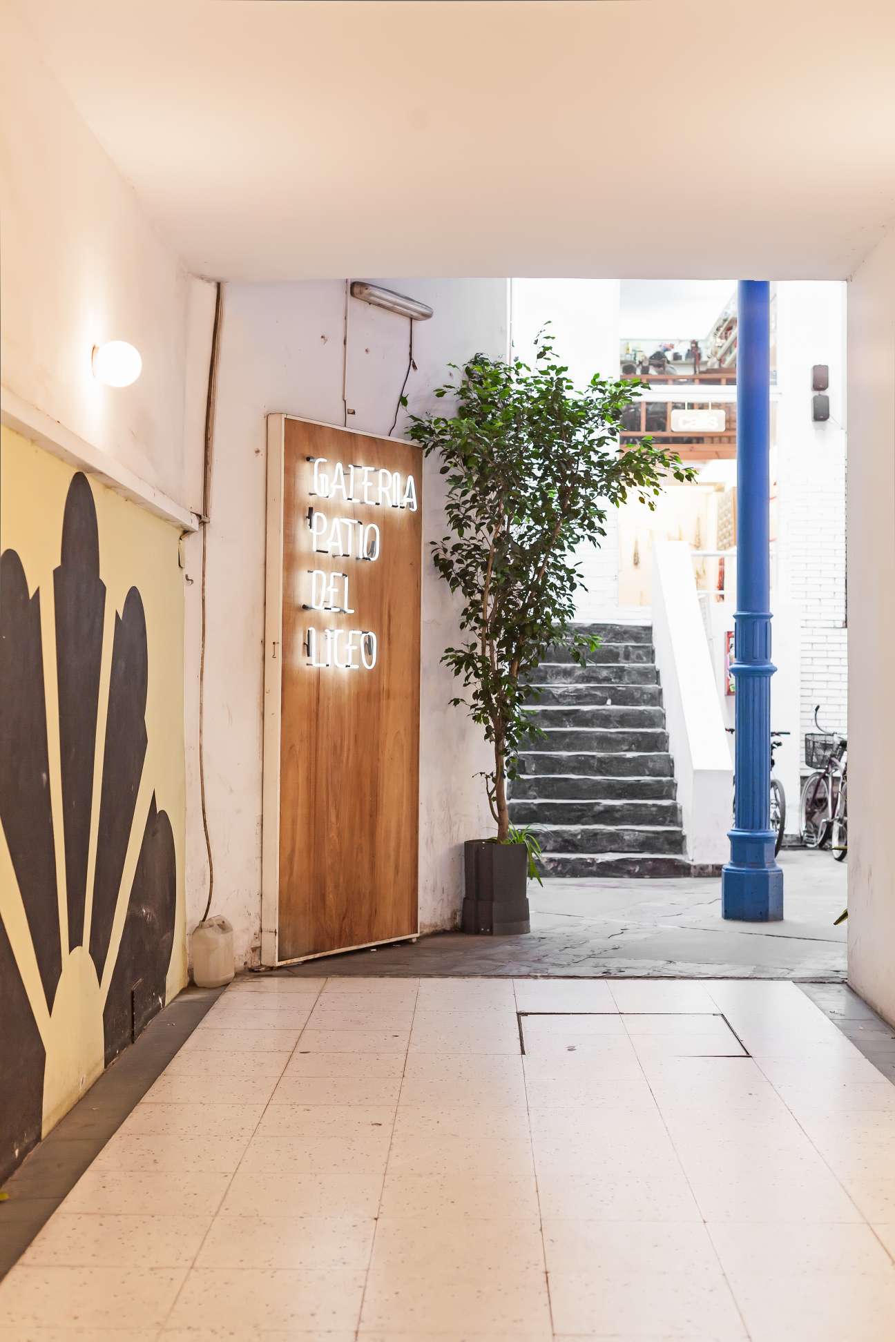 Entrance to Galería Patio del Liceo with neon sign, yellow wall art, and blue pillar in Buenos Aires.