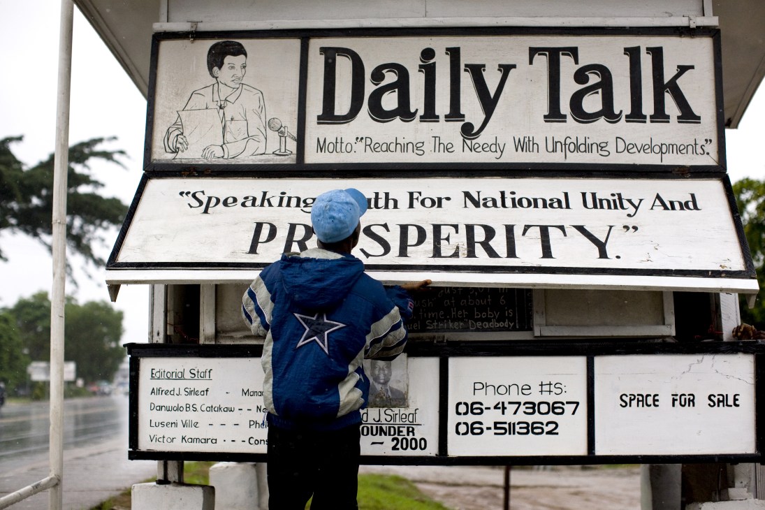A person in a blue jacket reads the Daily Talk blackboard newspaper in Monrovia, Liberia.