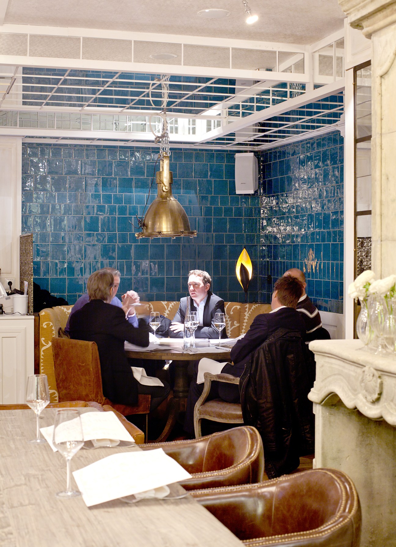 Restaurant interior with diners at table, blue tiled walls and brass pendant light.