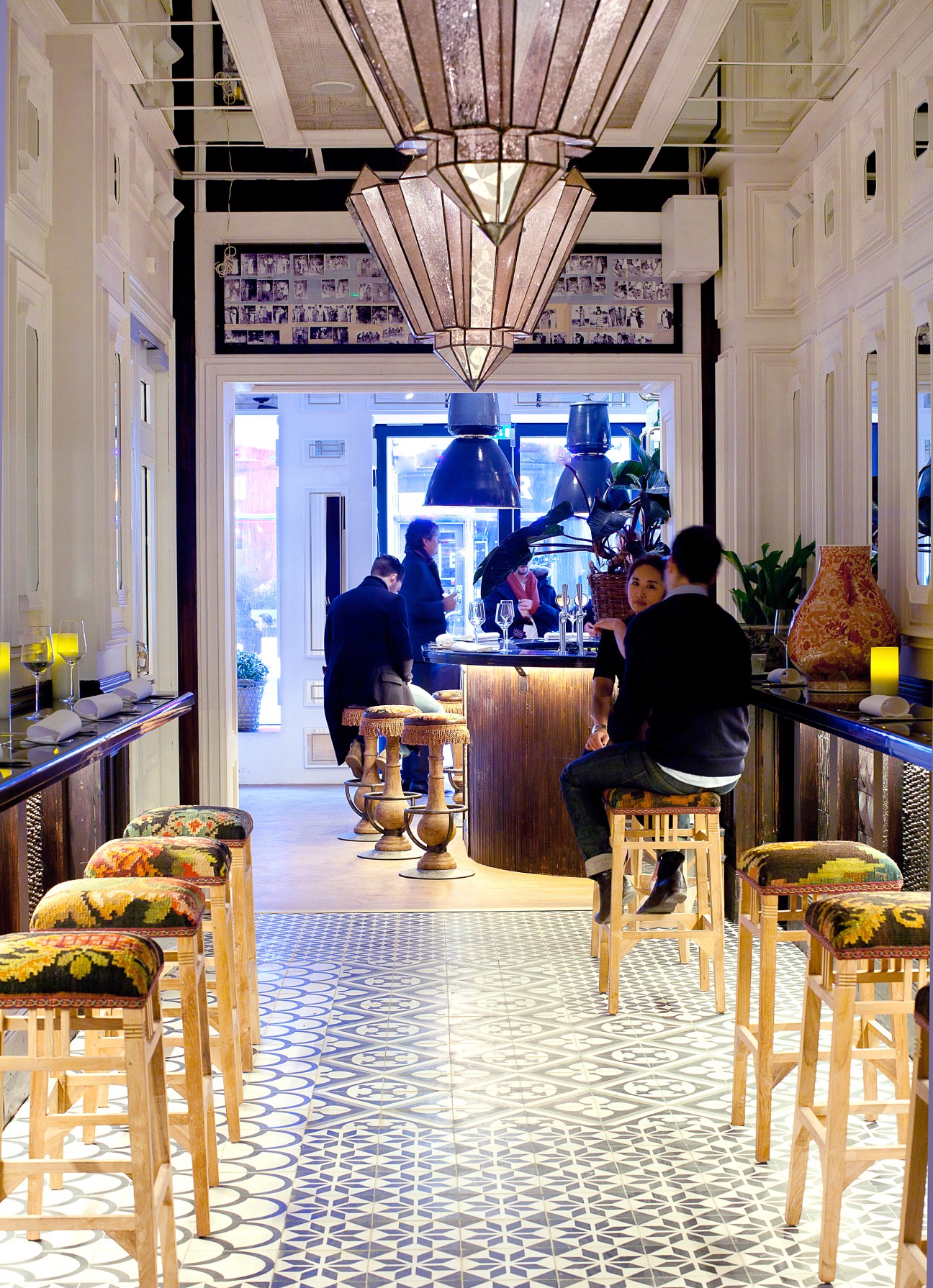 Interior of Nosh and Chow restaurant in Stockholm with geometric patterned flooring, wooden chairs with colorful cushions, and an art deco-style pendant light fixture.
