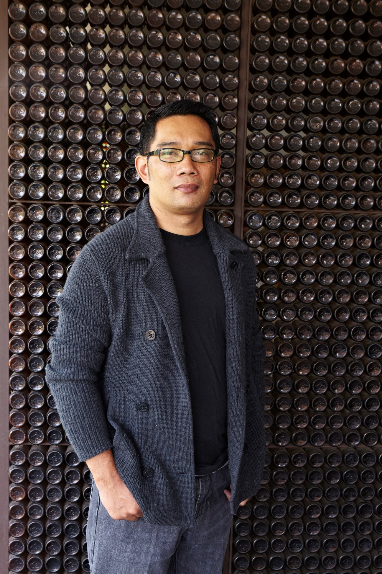 Architect and urban planner Ridwan Kamil poses against a textured wall of dark spheres.