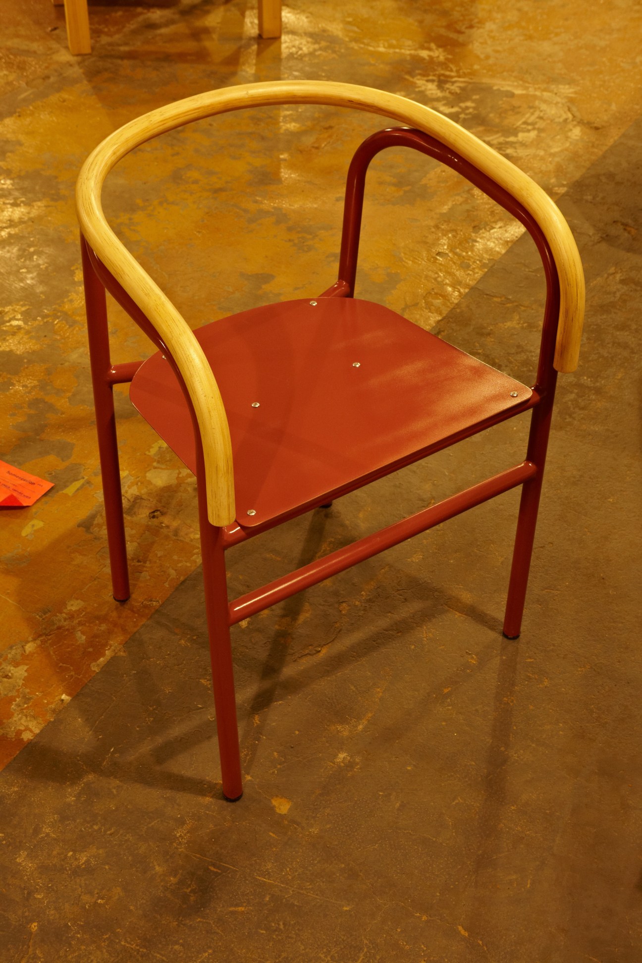 Modern wooden and red metal chair with curved armrests displayed in UNKL347 warehouse.