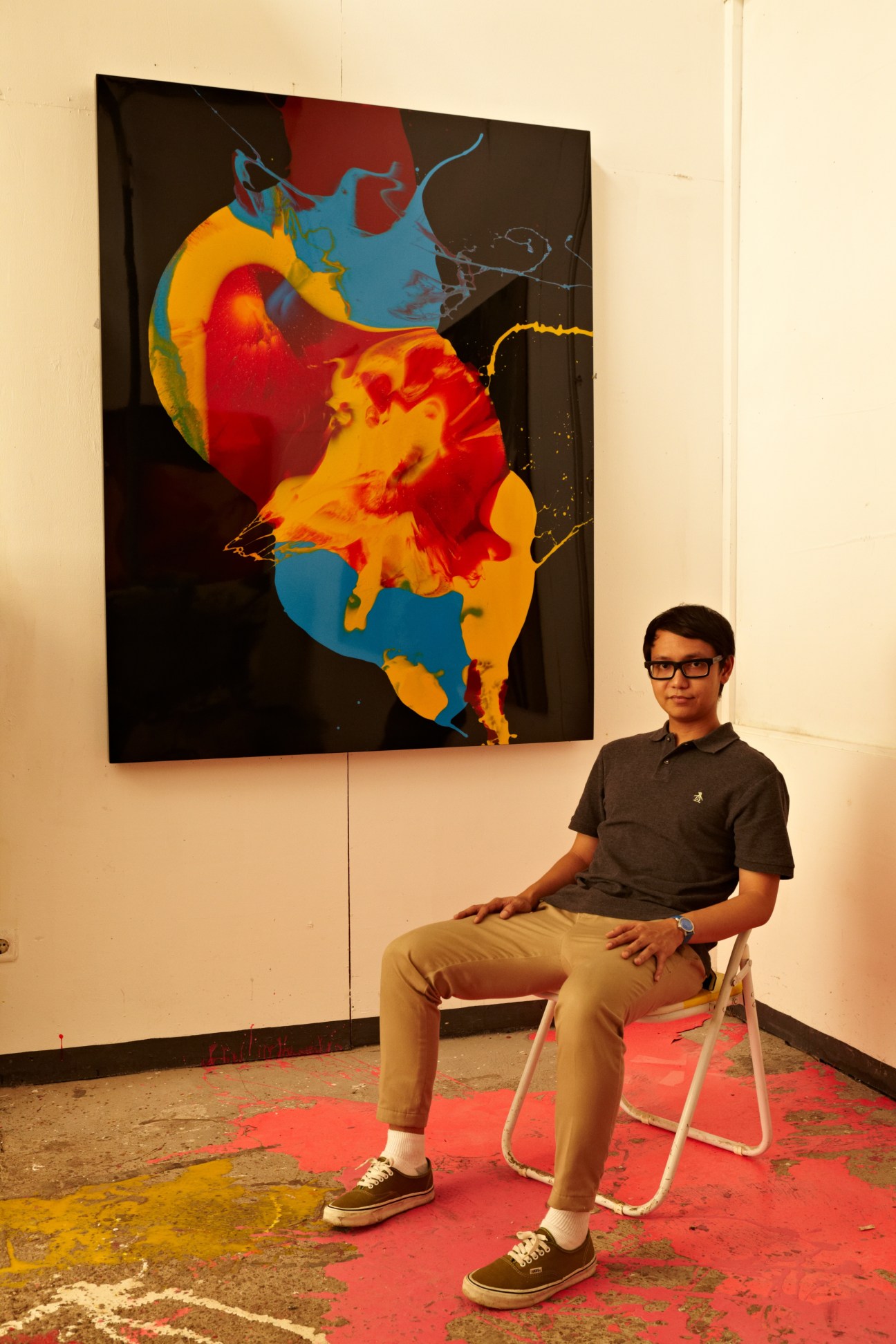 Bandung artist Arin Dwihartanto Sunaryo sitting in front of a colorful abstract painting in his studio.