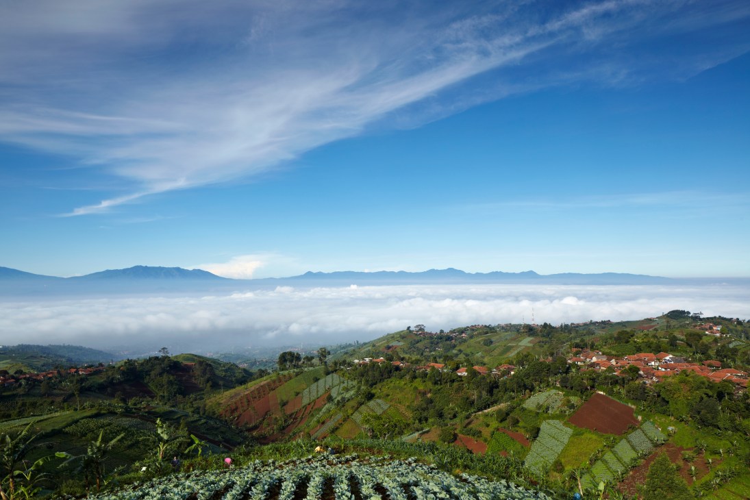 Bandung's volcanic basin landscape with fertile green hills, red-roofed houses, and distant mountains under blue sky.