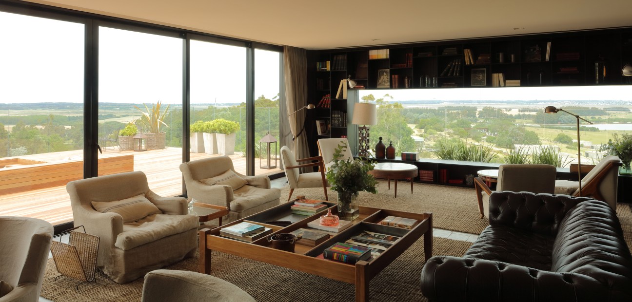 Modern hotel lounge with cream armchairs, dark shelving, panoramic windows overlooking landscape at La Locanda Fasano.