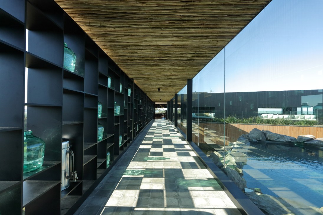 A covered corridor with chequered flooring and dark shelving displays a pool and rocky landscape beyond.