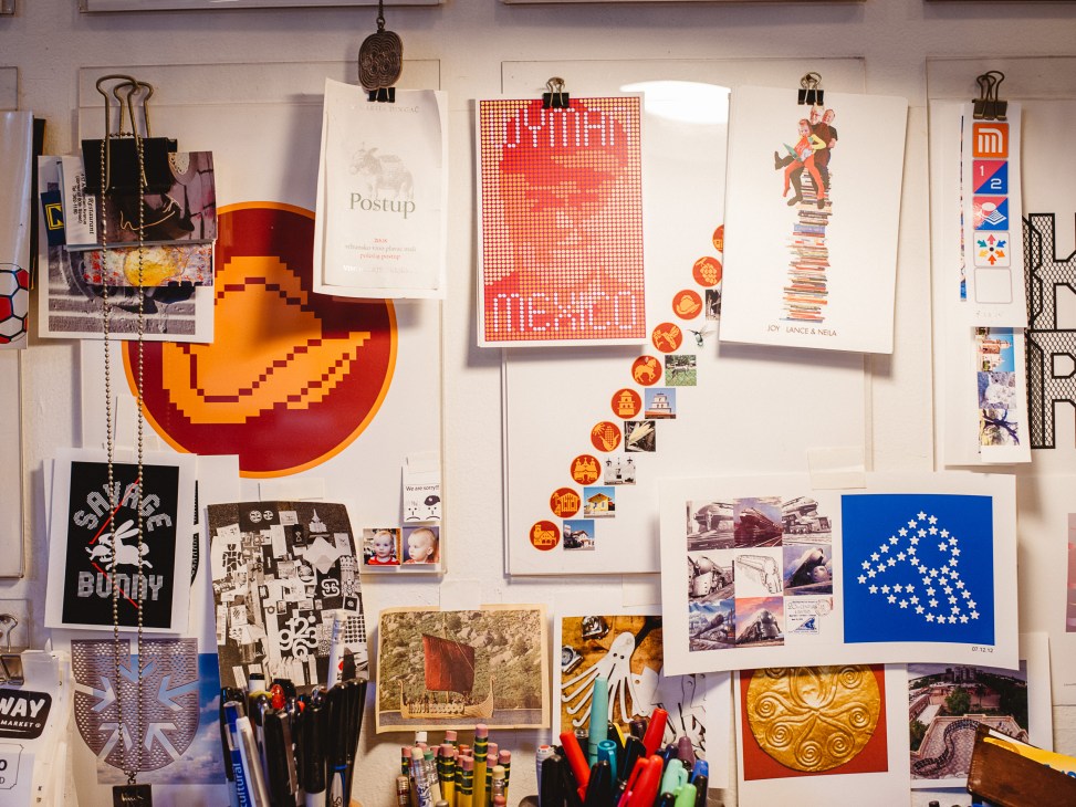 Mood boards and design samples pinned to a studio wall, including posters, geometric shapes, and color studies.