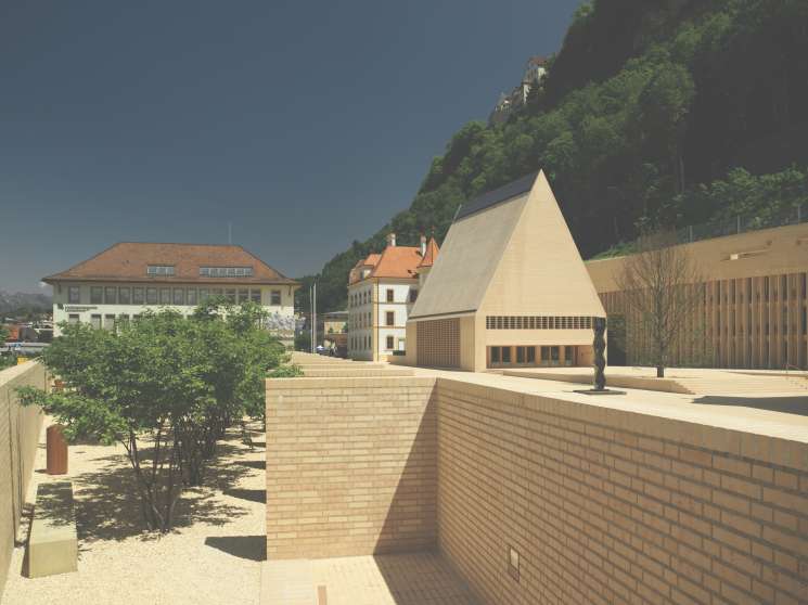 Liechtenstein's parliament building with steeply pitched roof alongside historic government buildings in an Alpine setting.