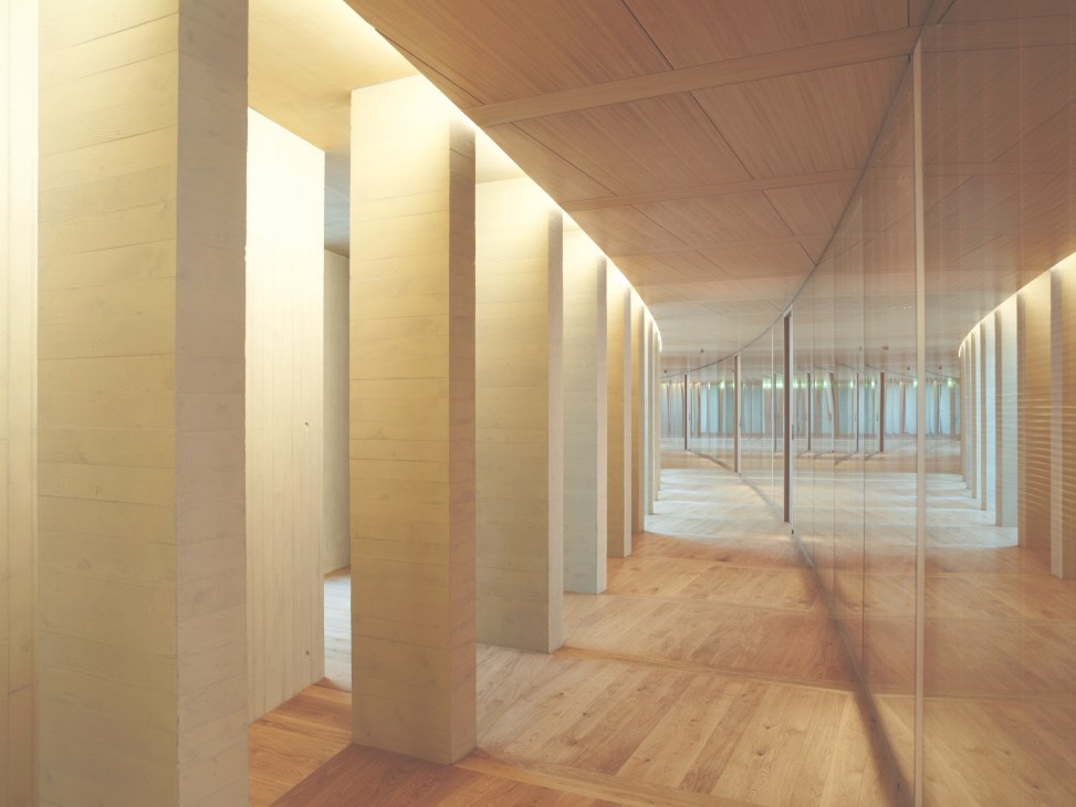 A formal corridor with brick columns, wooden flooring, and glass partitions lit by warm ambient lighting.