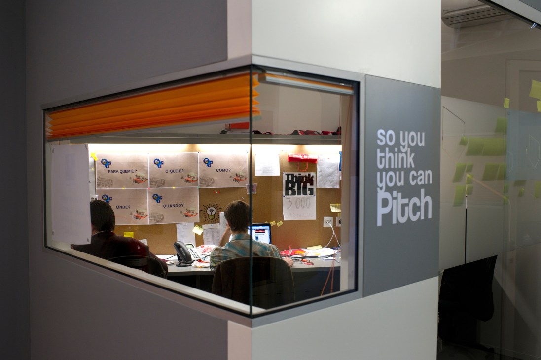 Interior view of Factory Work Style co-working space in Portugal with entrepreneurs working at desks displaying startup pitch materials.