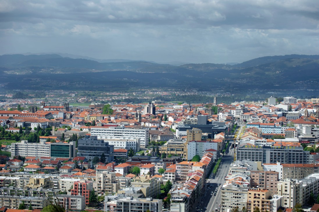 Aerial view of Braga, Portugal showing the city's historic center with red-tiled roofs and mountains in the background.