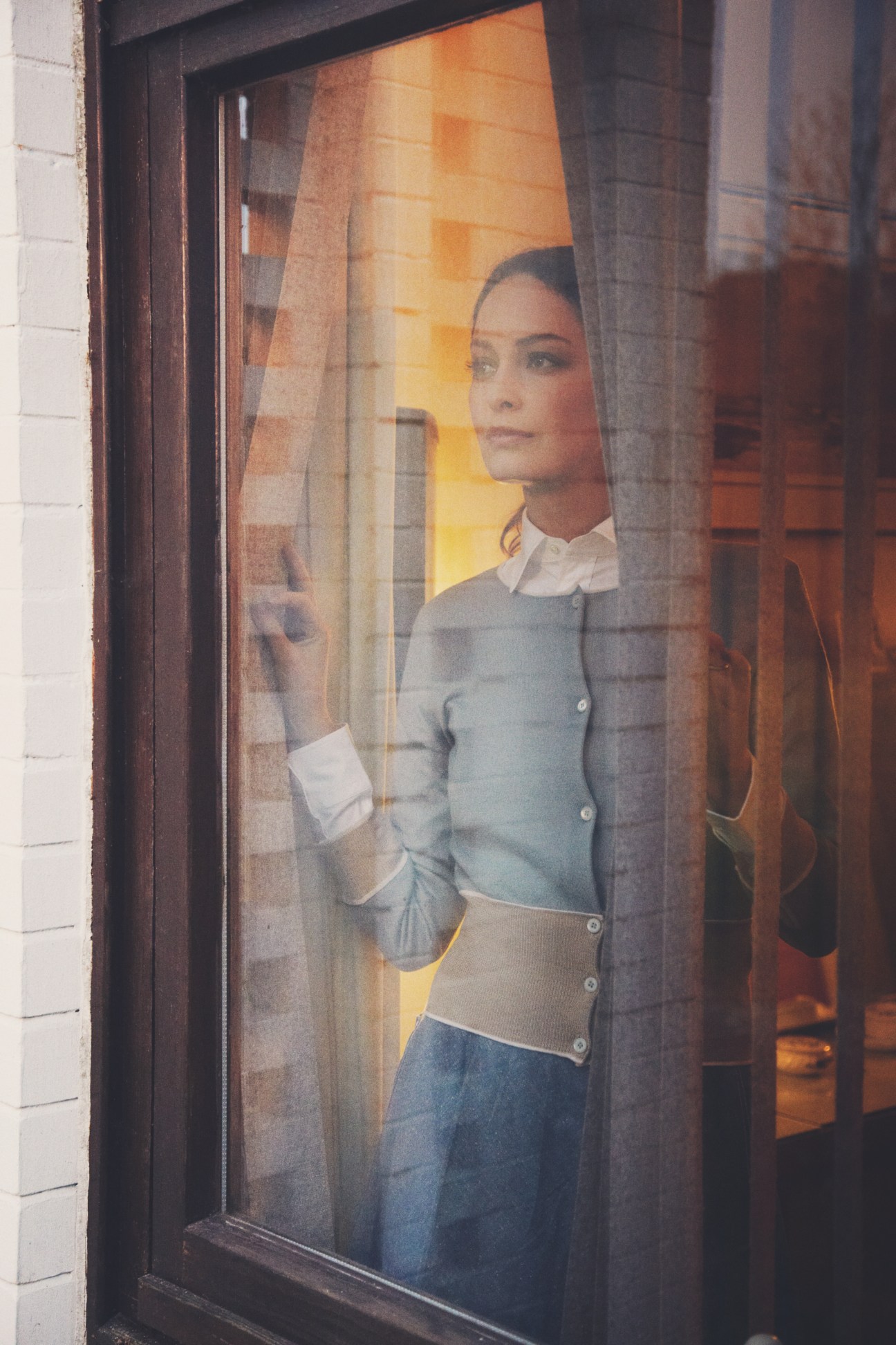 Woman wearing Prada cardigan, Ralph Lauren shirt, and G-Star skirt, looking out through a window.
