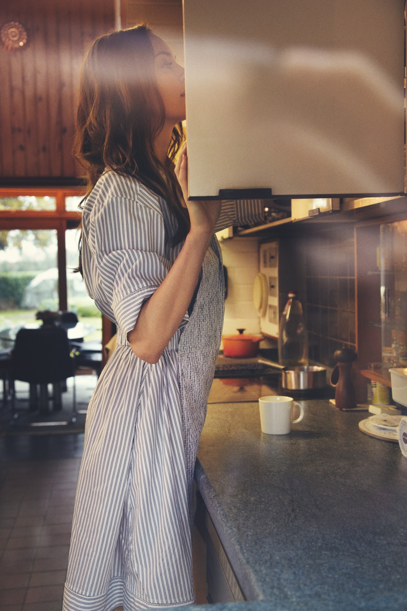 Woman wearing a striped Fendi dress in a modern kitchen with mid-century architecture visible through windows.