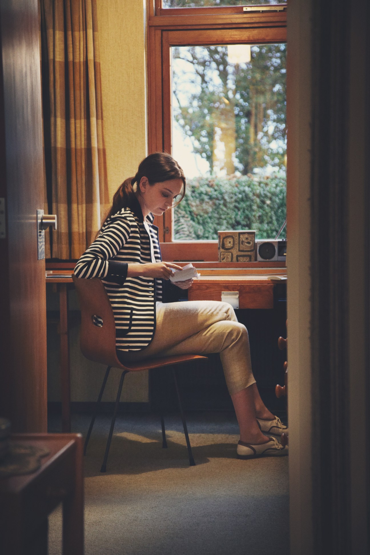 Woman in striped Gucci shirt and Woolrich jacket sitting at desk in modernist interior
