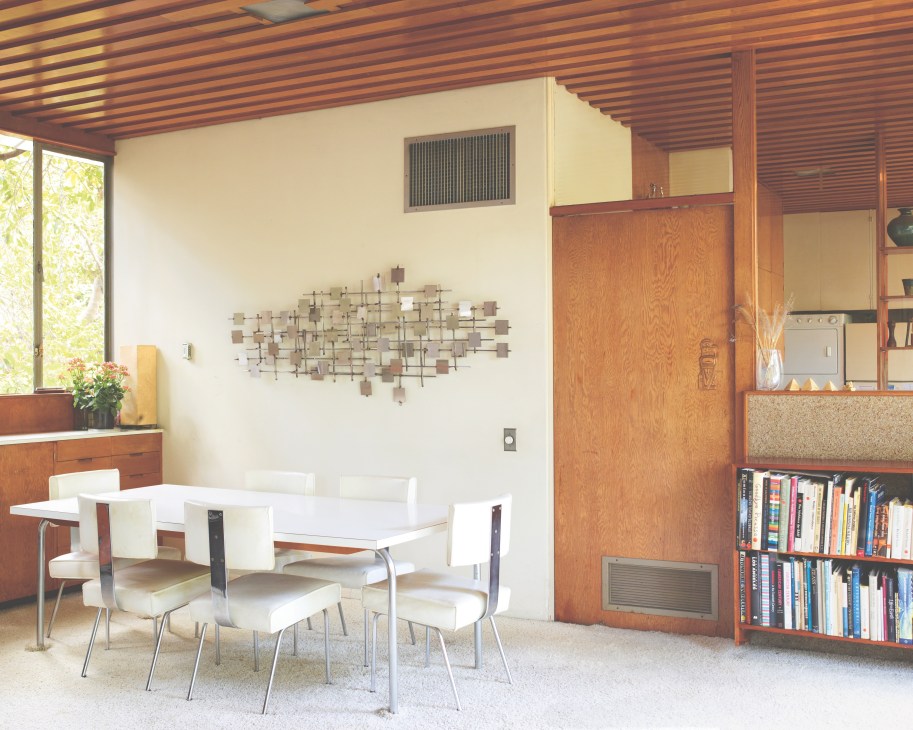 Mid-century modern dining area with white chairs and table designed by Richard Neutra, wooden ceiling, and built-in shelving.