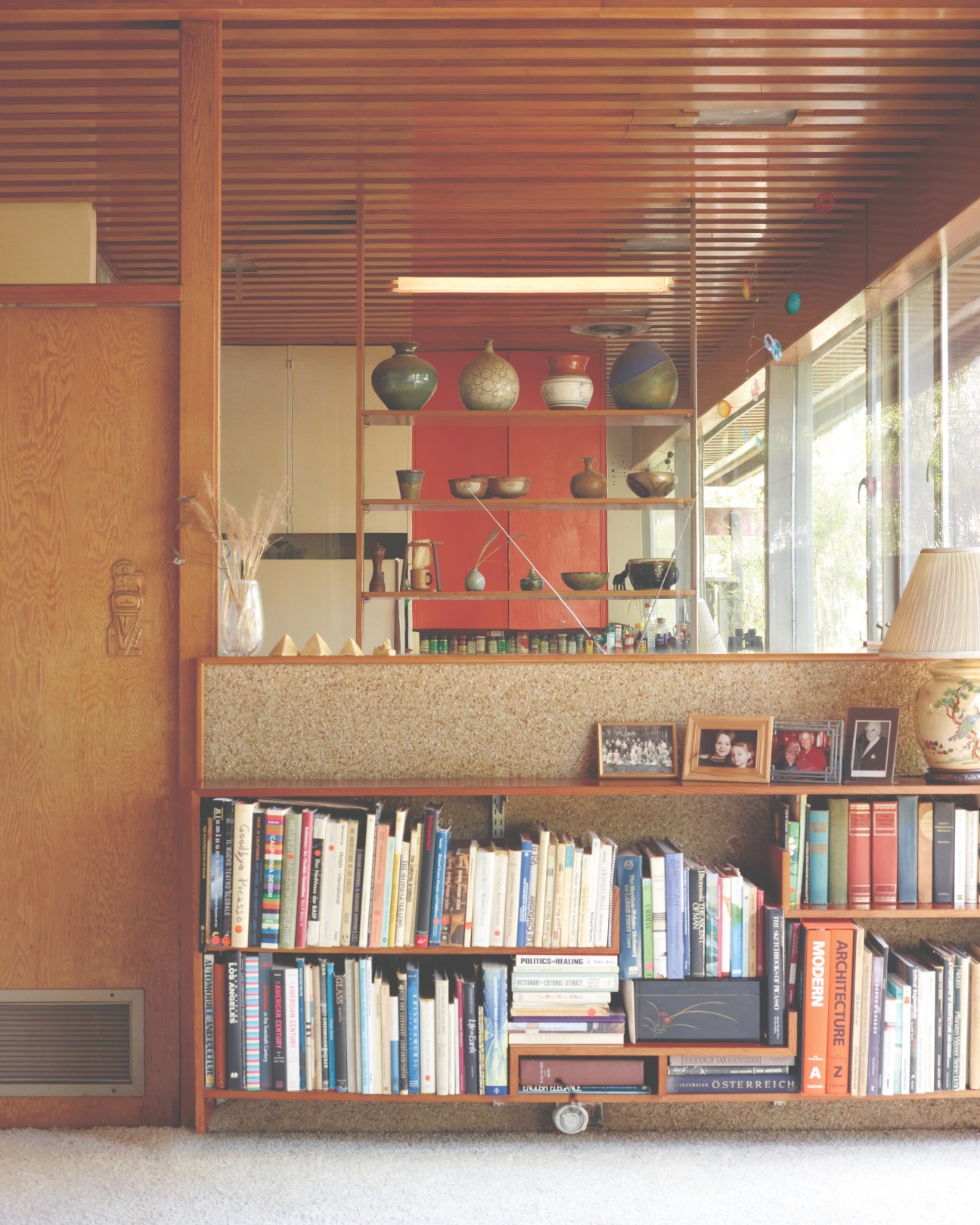Built-in wooden shelving with red backing divides interior spaces, displaying books and decorative objects.