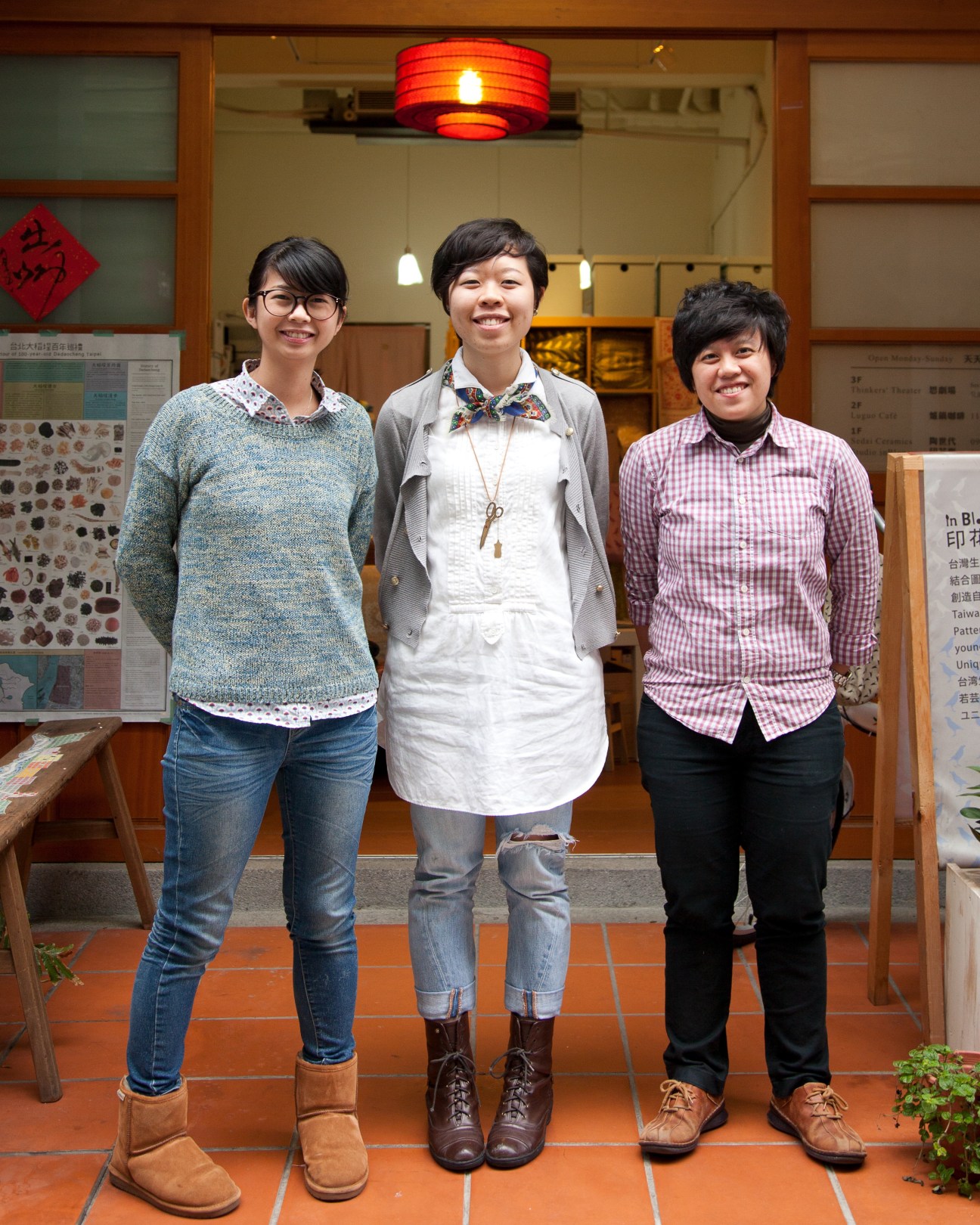 Three smiling women stand in front of Art Yard shop entrance with red lantern and wooden storefront.