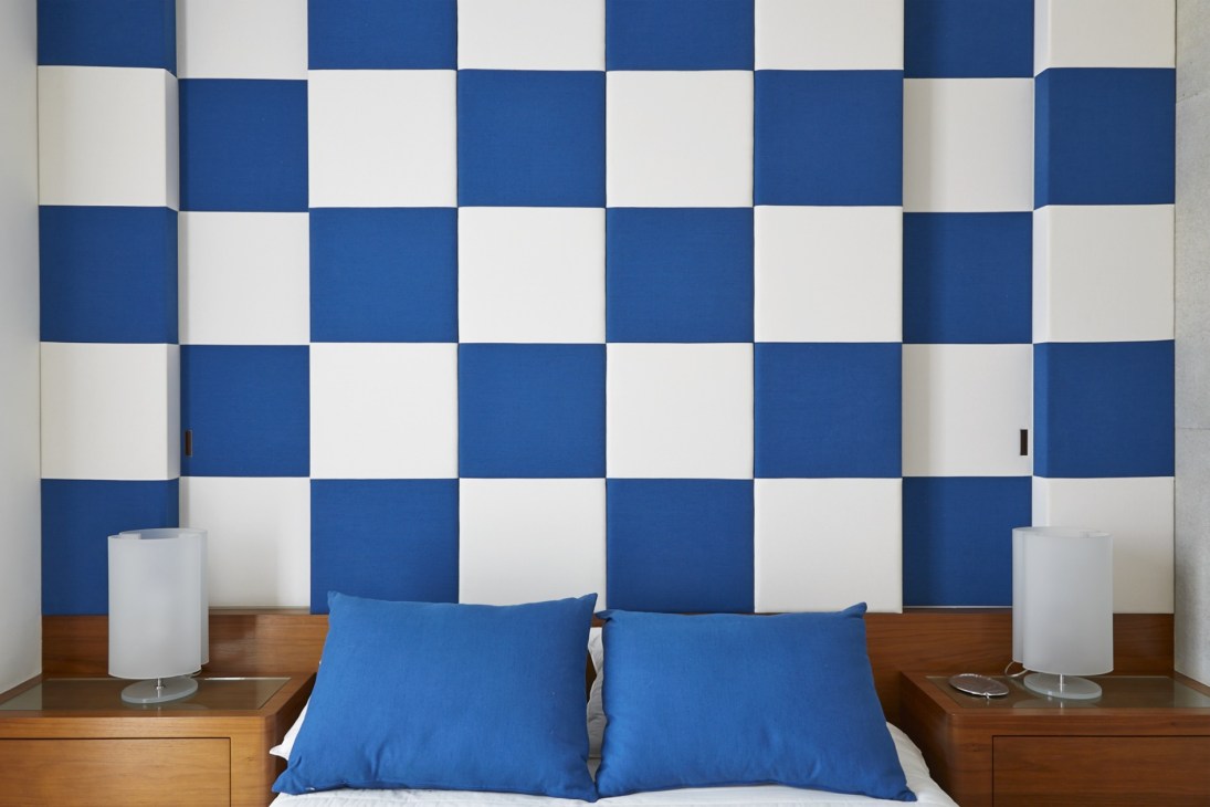 Bedroom with blue and white checkered wall pattern, wooden nightstands, blue pillows, and modern cylindrical lamps.