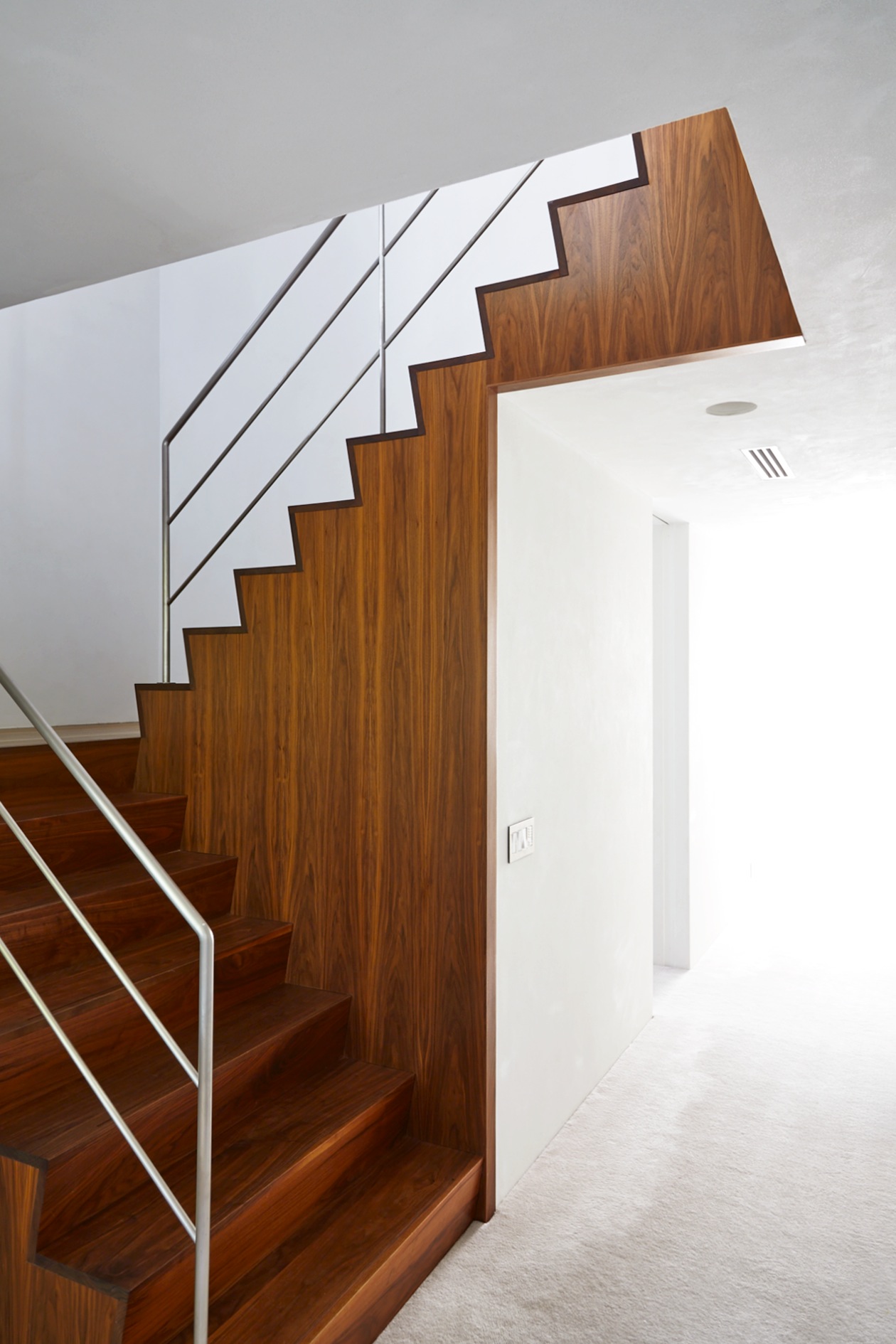 Modern wooden staircase with metal railing against white wall in bright interior space.