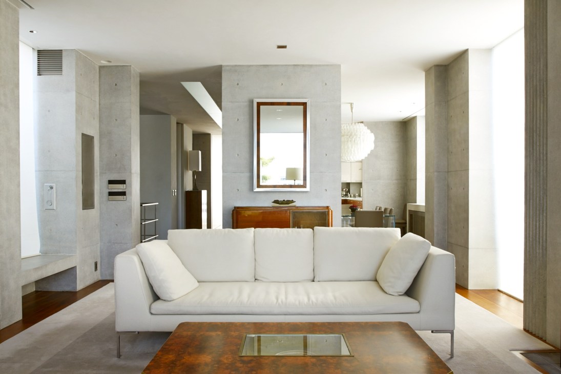 Modern living room with white sofa, concrete walls, wooden furniture and framed mirror by Hiroshi Seki.